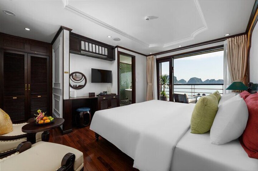 A modern hotel room with a large bed, a TV, a desk with a chair, and a view of the sea. 5