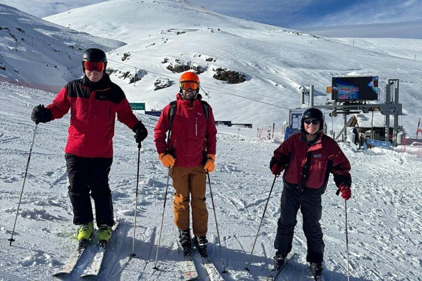 Three skiers on a snowy slope with ski equipment, a ski lift, and a clear sky. 5