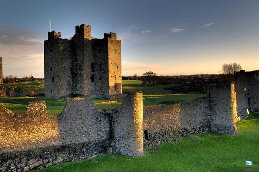 Un castillo medieval con una gran torre, rodeado por un campo cubierto de hierba y muros de piedra. 3