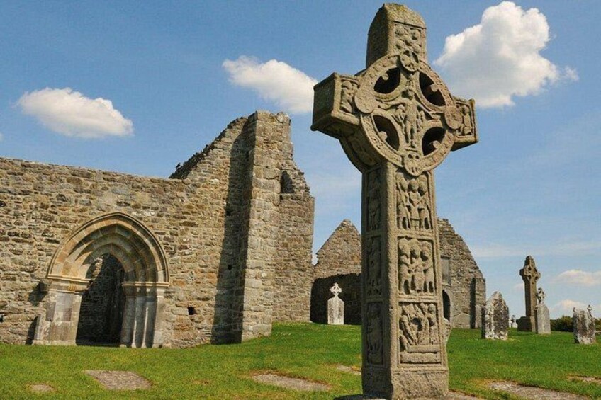 Una iglesia de piedra con una gran cruz, ruinas y un campo cubierto de hierba. 5