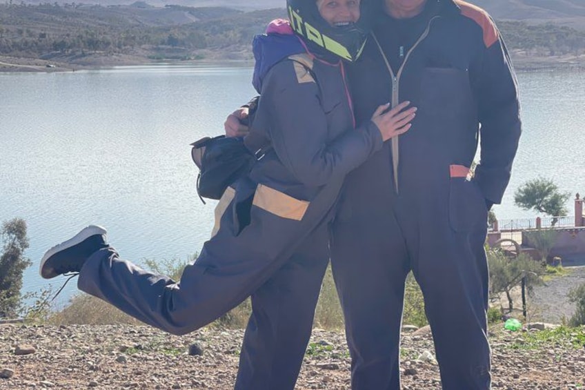 Twee mensen in outdoor kleding aan een meer, met een heuvelachtig landschap op de achtergrond. 2