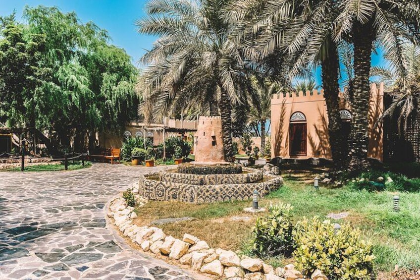 A courtyard with palm trees, a stone pathway, and a small tower-like structure. 3