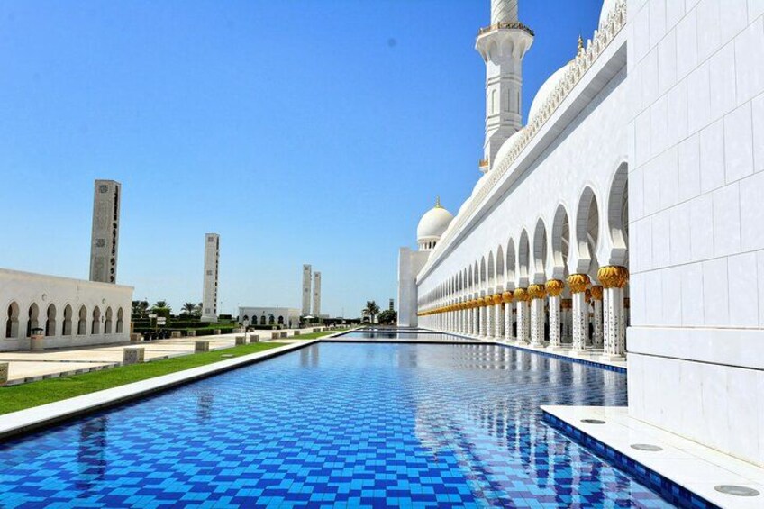 A swimming pool with blue tiles, white buildings with arches, and a clear blue sky. 5