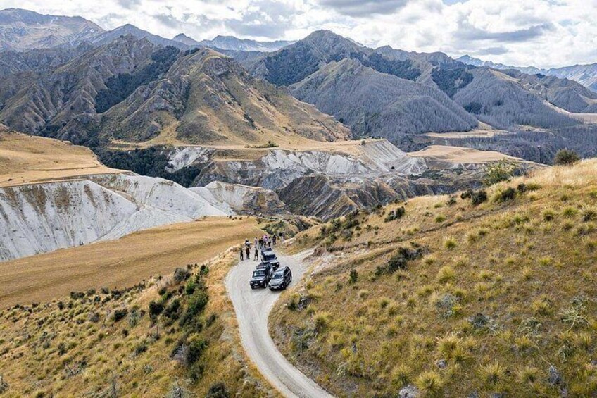 A winding road through a mountainous landscape with a group of vehicles and people. 5
