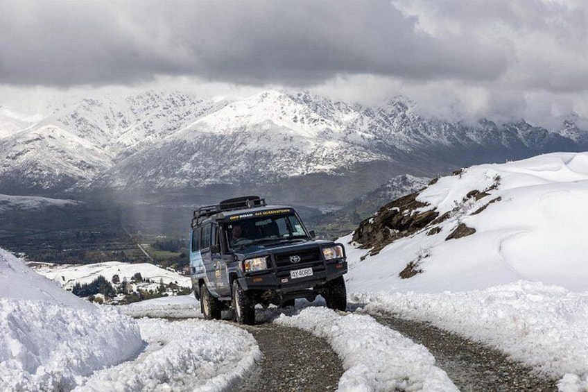A vehicle on a snow-covered path with mountains in the background. 2