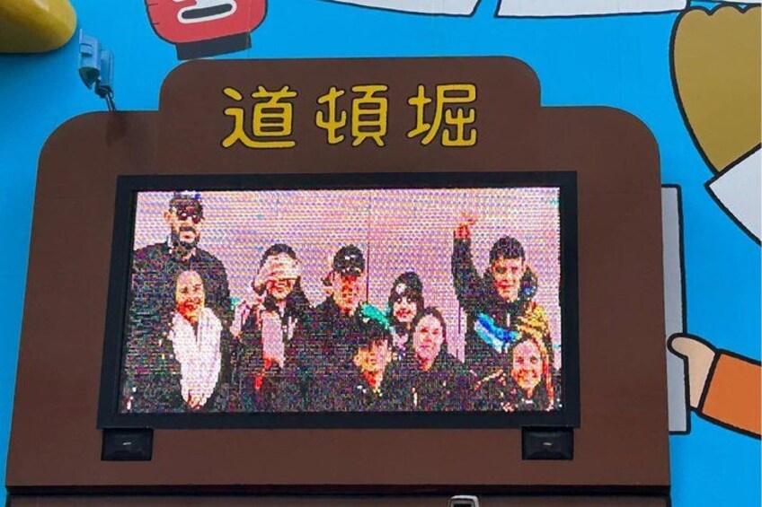 Una pantalla digital muestra a un grupo de personas, un letrero con caracteres chinos y un personaje de caricatura. 4