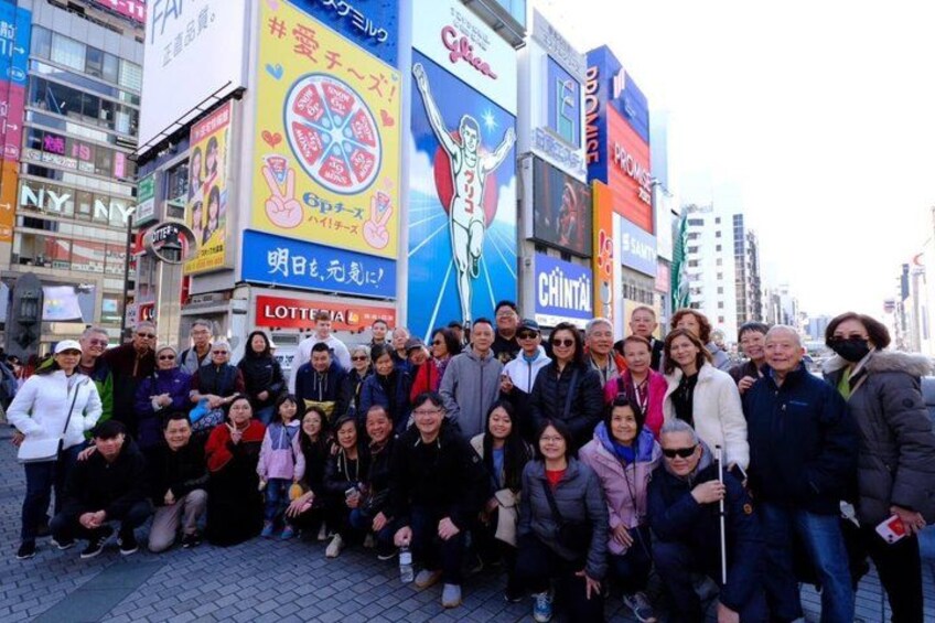Un grupo de personas posando en una concurrida calle urbana, con grandes anuncios y escaparates. 5
