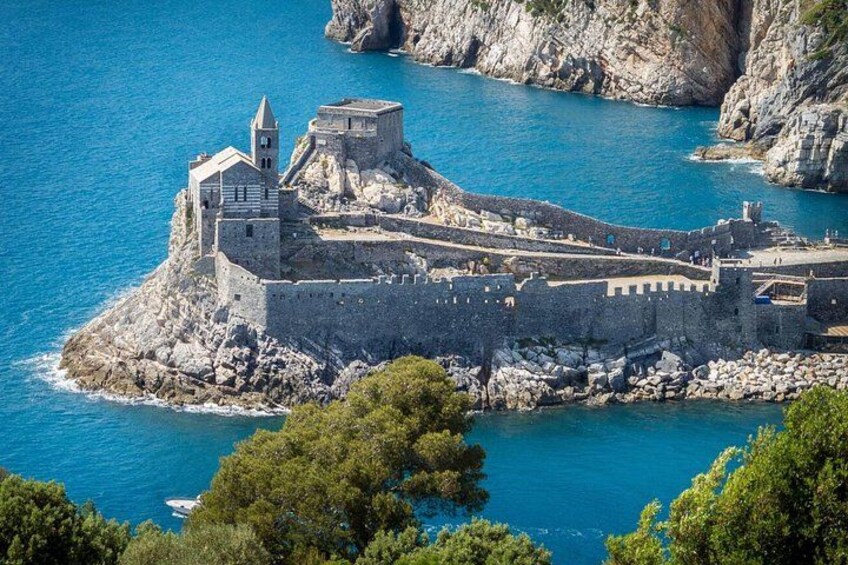 A fortified coastal castle with a prominent tower, surrounded by rocky cliffs and clear blue waters. 1