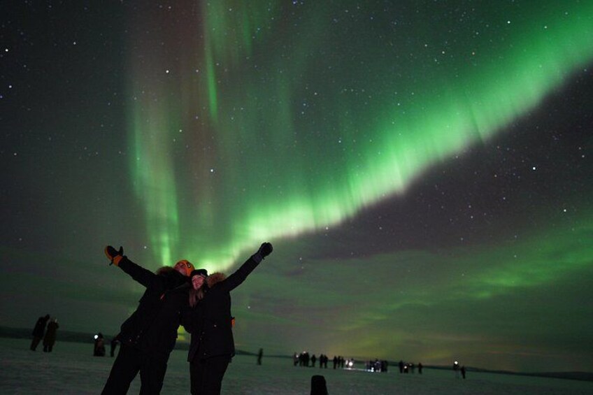 A person with arms raised, a person in a yellow hat, and a crowd of people under a night sky with green aurora. 1