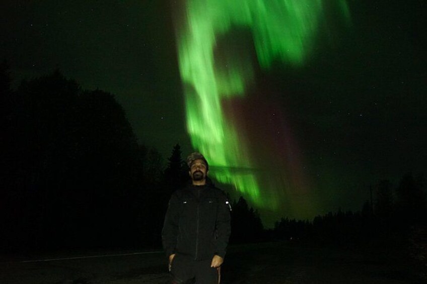 A person standing in a dark landscape with the Northern Lights in the background. 4