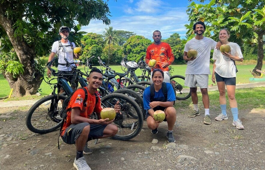 A group of people holding coconuts, with bicycles in the background. 5