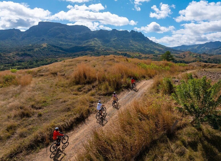Three cyclists on a dirt trail in a hilly landscape with mountains in the background. 5