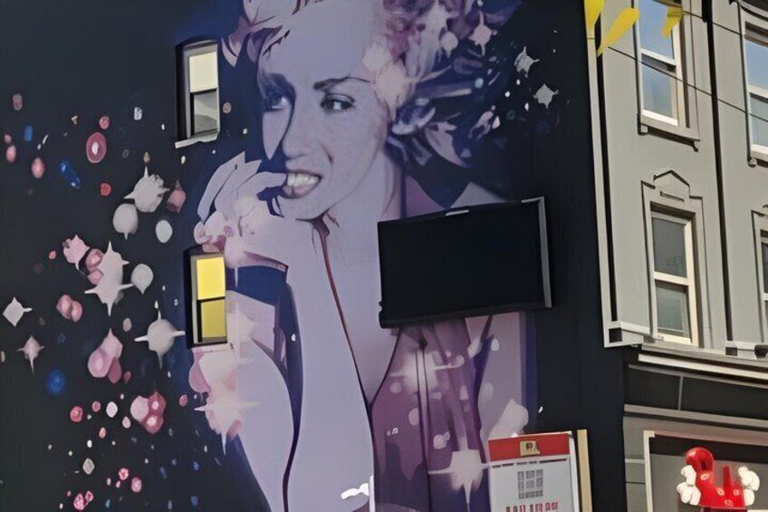 A building with a mural of a woman holding a drink, a blackboard, and a red sculpture. 2