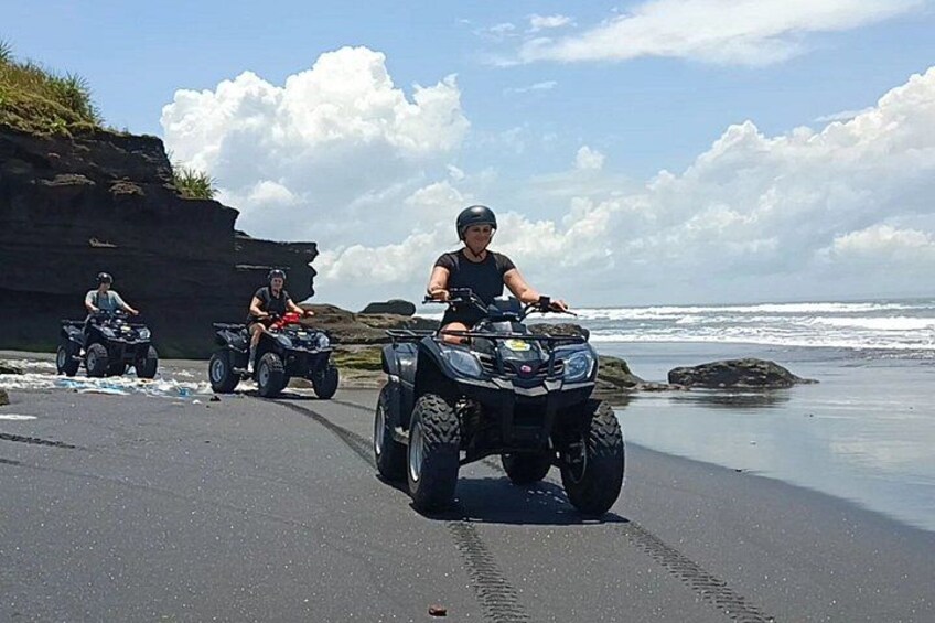 Three people riding ATVs on a beach with ocean waves in the background. 1