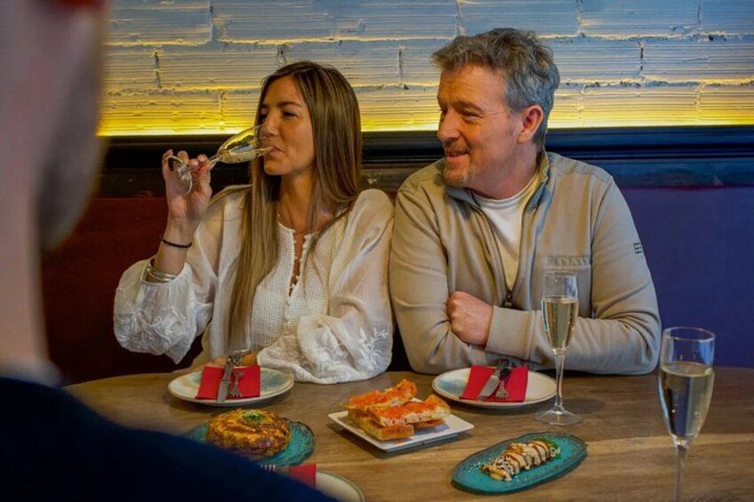 Two people sitting at a table with plates of food and glasses of wine. 1