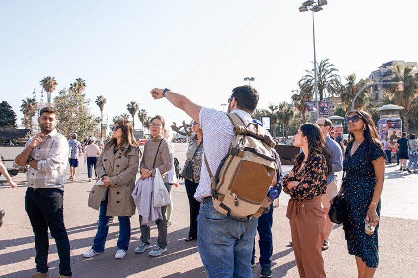 A group of people standing outdoors, some with backpacks, in a sunny urban setting with palm trees and buildings in the background. 5