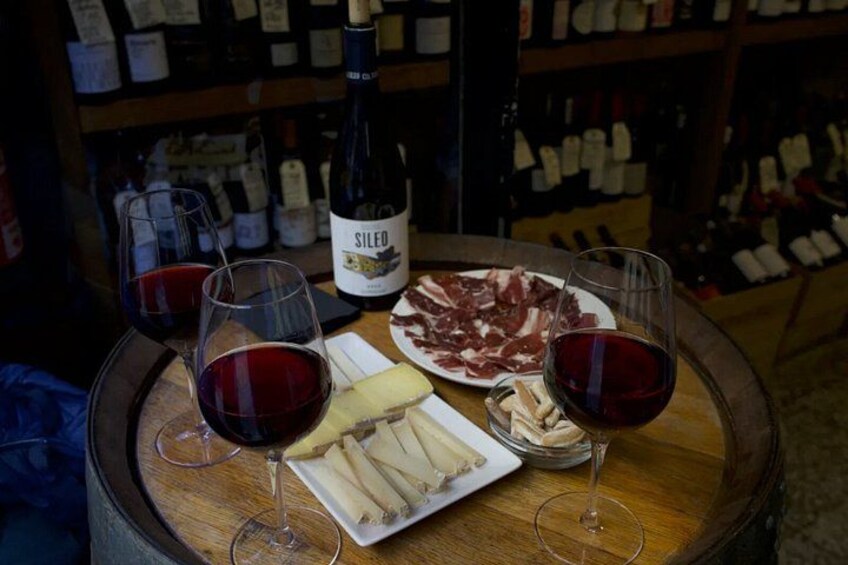 A wine bottle labeled 'SILEO' on a table with glasses of red wine, plates of cheese, and cured meats. 2