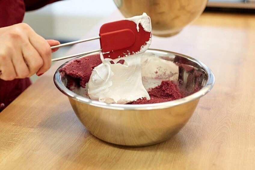 A person mixing ingredients in a metal bowl with a red spatula. 5
