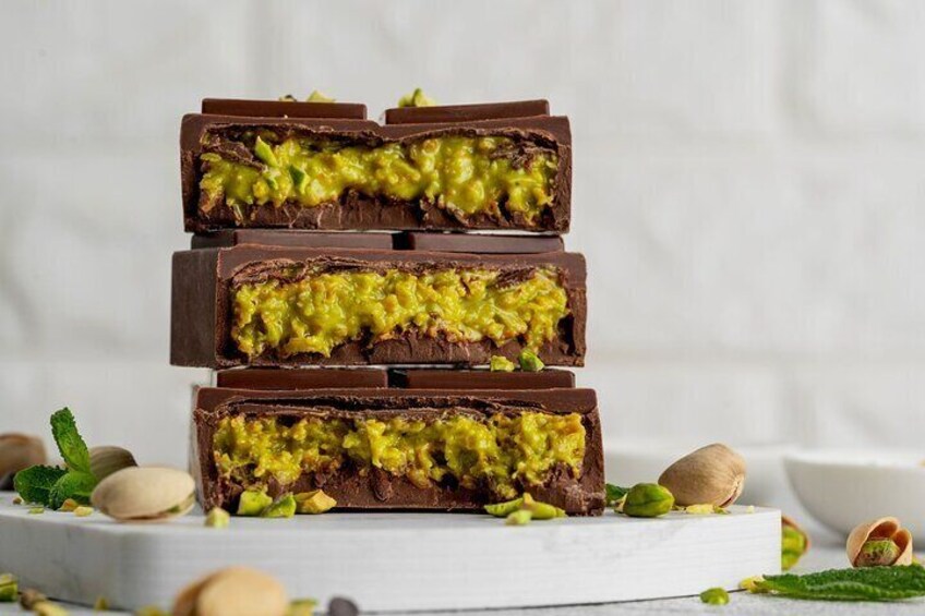 Een stapel chocoladerepen met groene vulling, omringd door pistachenoten en muntblaadjes. 1
