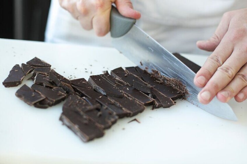 Iemand snijdt chocolade in stukken op een wit snijplank. 2