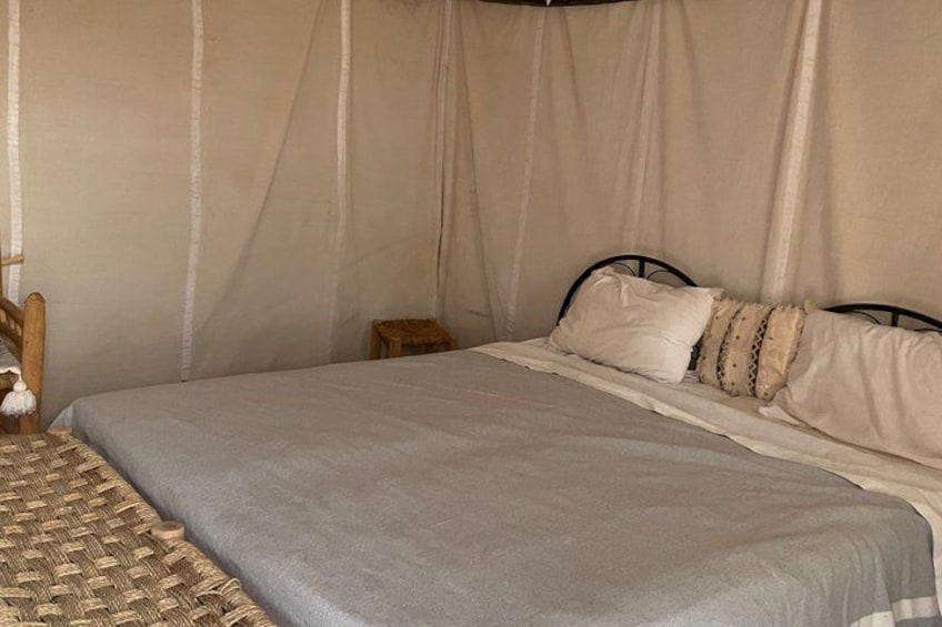 A bed with a grey blanket, a wooden headboard, and a small wooden stool. 3