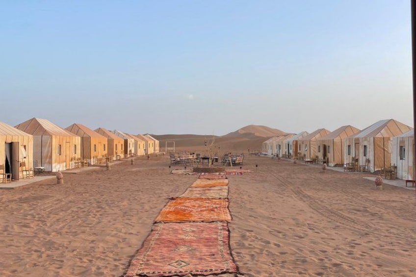 A desert landscape with multiple tents aligned in rows, a sandy ground, and distant hills. 2