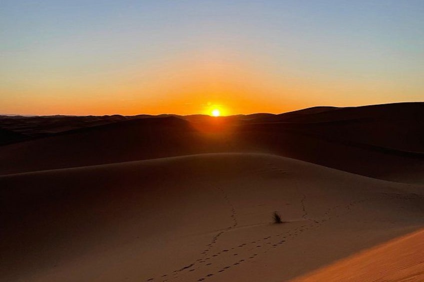 A desert landscape with a sunset, sand dunes, and a person walking. 1