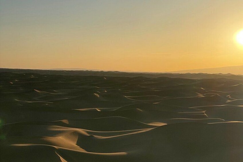 A desert landscape with undulating sand dunes under a clear sky. 4