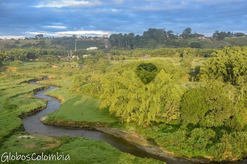 A river winding through lush green fields, with trees and a distant wind turbine. 2