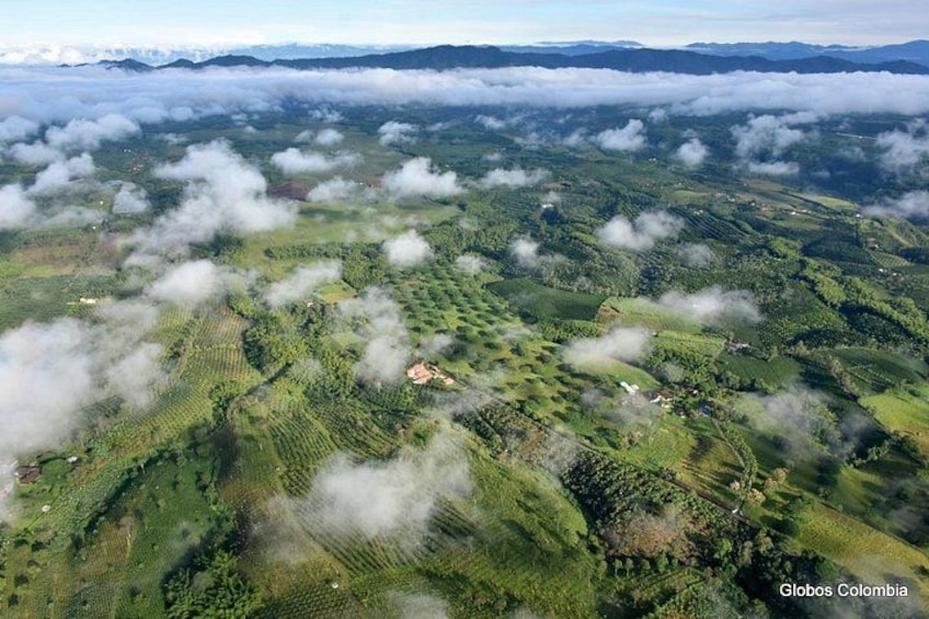 A mountainous landscape with patches of clouds, green fields, and scattered buildings. 3