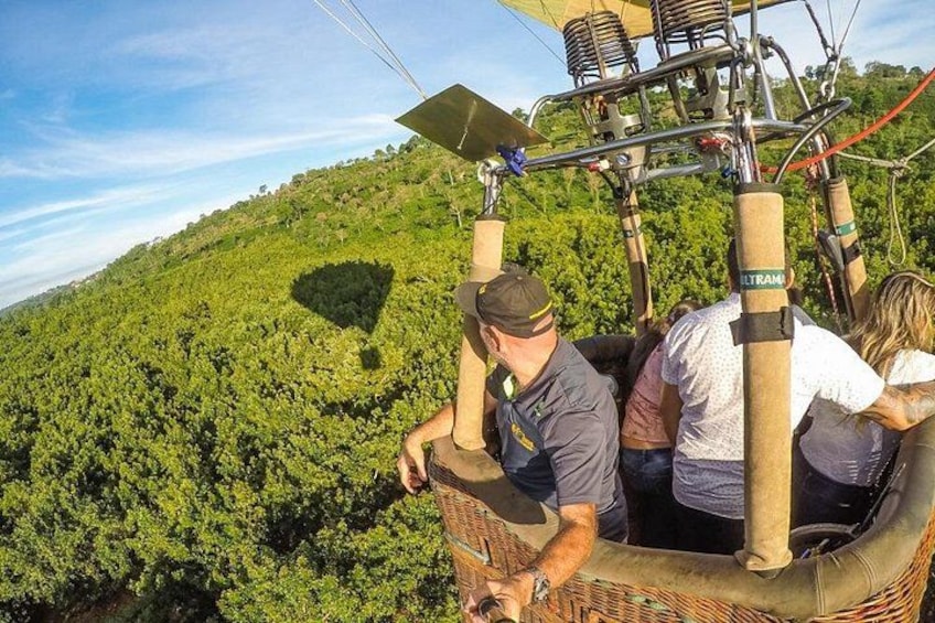 A hot air balloon with passengers, a wicker basket, and a lush green landscape below. 5