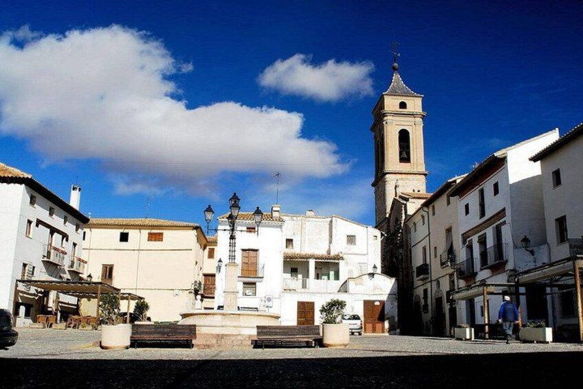 A town square with a central fountain, a clock tower, and surrounding buildings. 4