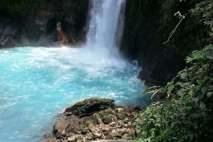 Una cascada se precipita en una piscina turquesa rodeada de rocas y follaje. 1