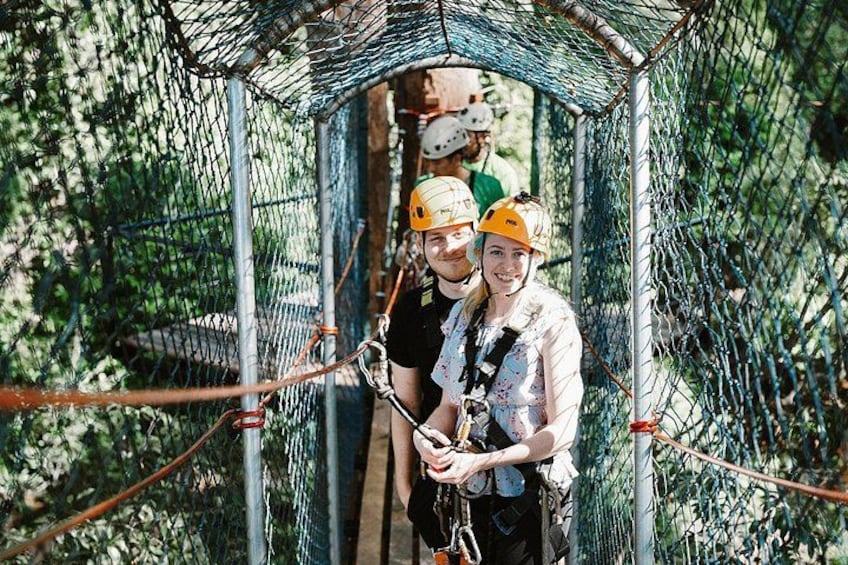 A rope bridge in a forested area with people wearing helmets and harnesses. 4