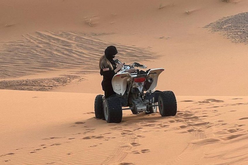 A person on a quad bike in a desert with sand dunes. 1
