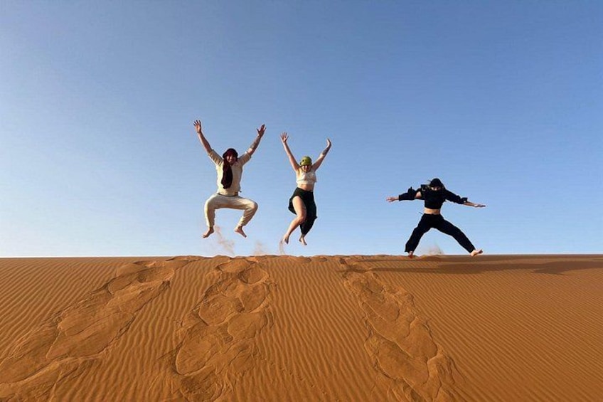 Three people jumping off a sand dune in a desert landscape. 1