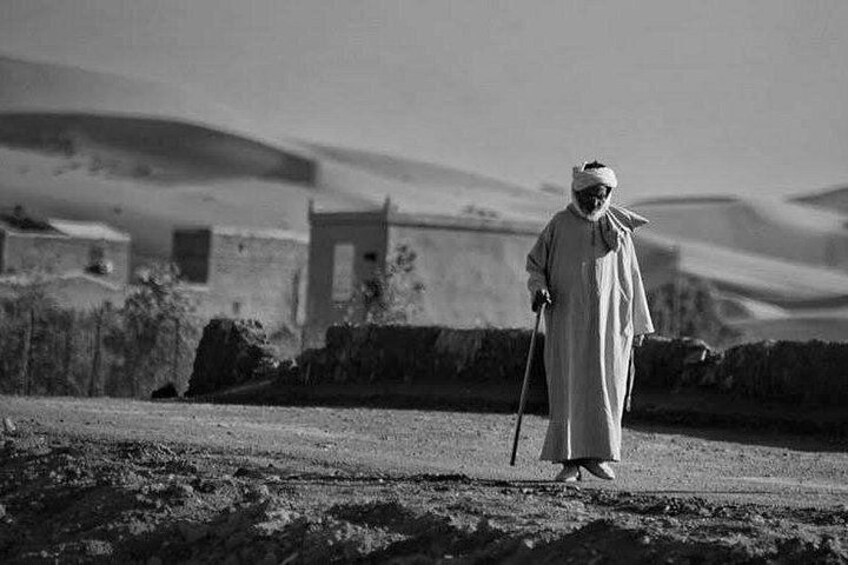 A person in traditional attire walking on a desert path with buildings in the background. 5