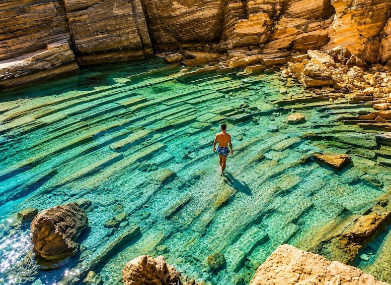 A person walking on a rocky beach with clear water. 1
