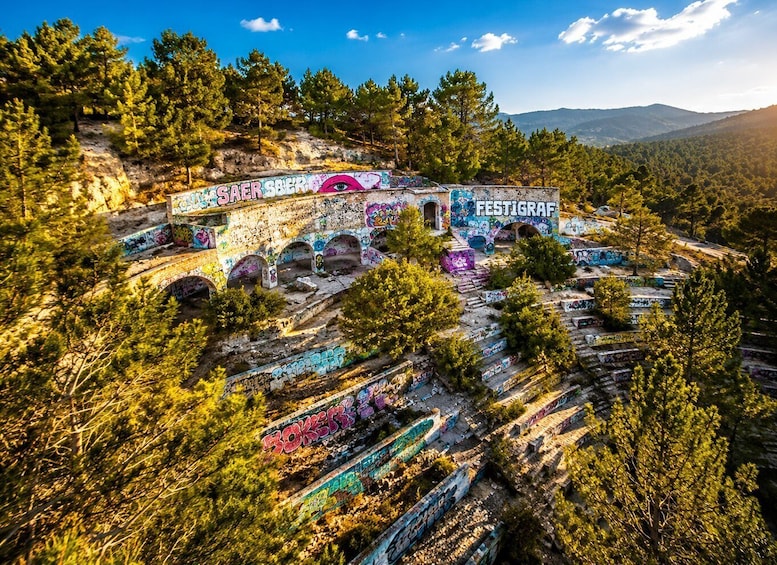 A mountainous landscape with graffiti-covered ruins and dense forest. 5
