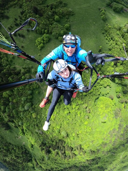 Two people skydiving over a lush green landscape. 1