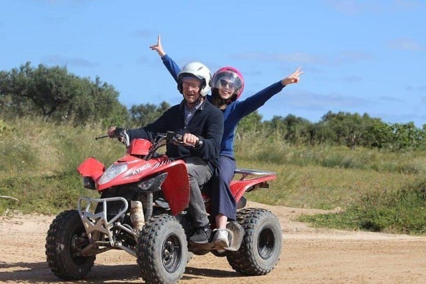 Dos personas en un vehículo todo terreno rojo sobre un camino de tierra, con vegetación al fondo. 2