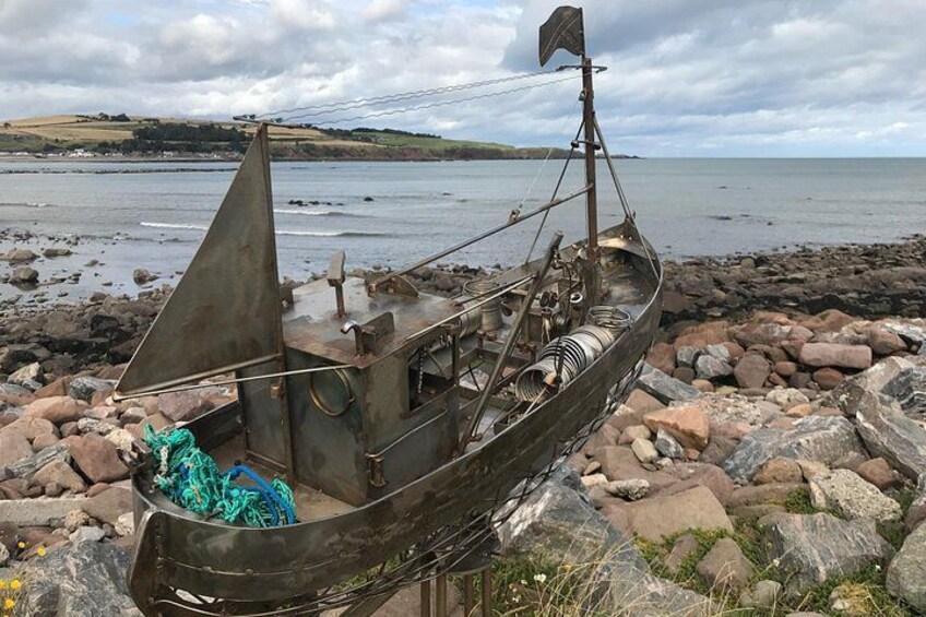 Un modelo de barco en una costa rocosa, con una masa de agua y colinas al fondo. 4