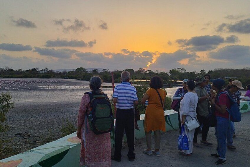 A group of people standing on a bridge overlooking a body of water during sunset. 3