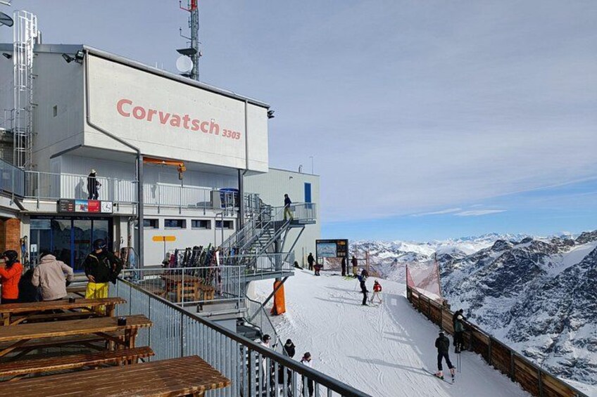 Une station de ski avec un bâtiment portant l’inscription « Corvatsch 3303 », des personnes qui font du ski et un paysage montagneux enneigé. 5