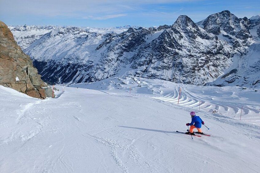 Un skieur sur une pente enneigée, avec des affleurements rocheux et des sommets enneigés en arrière-plan. 4
