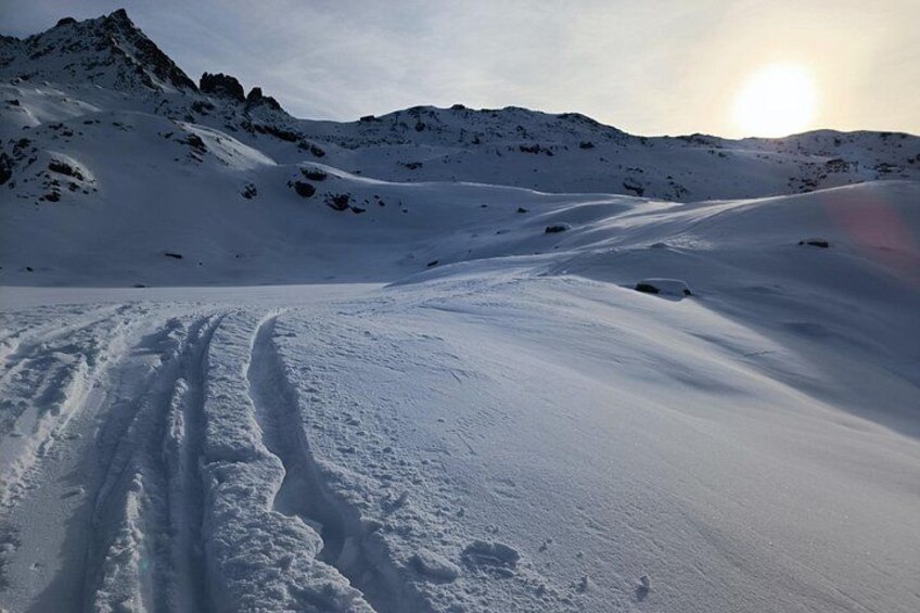 Un paysage montagneux enneigé, avec des traces de pneus et un soleil couchant à l’horizon. 2