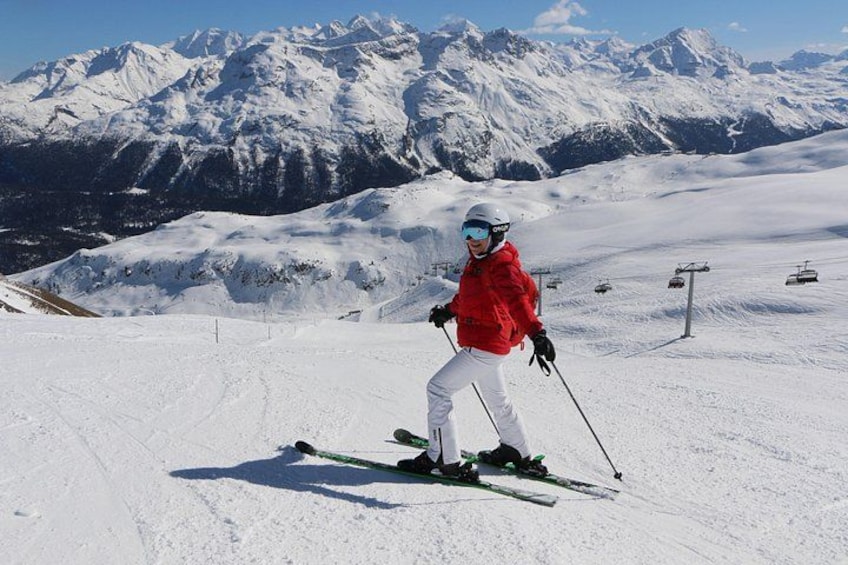 Un skieur, vêtu d’une veste rouge et d’un pantalon blanc, descend une pente enneigée, avec une chaîne de montagnes en arrière-plan. 1