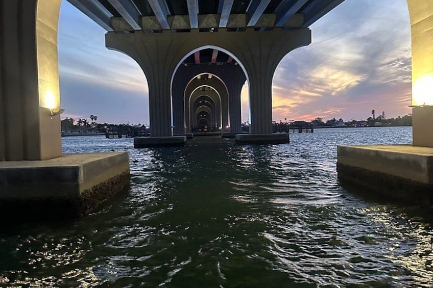 A bridge over water with multiple arches, a sunset in the background, and a calm sea. 2