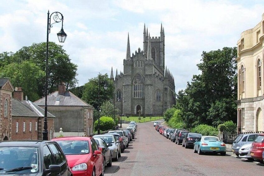 Calle con coches aparcados que conduce a una iglesia grande con una aguja. 3