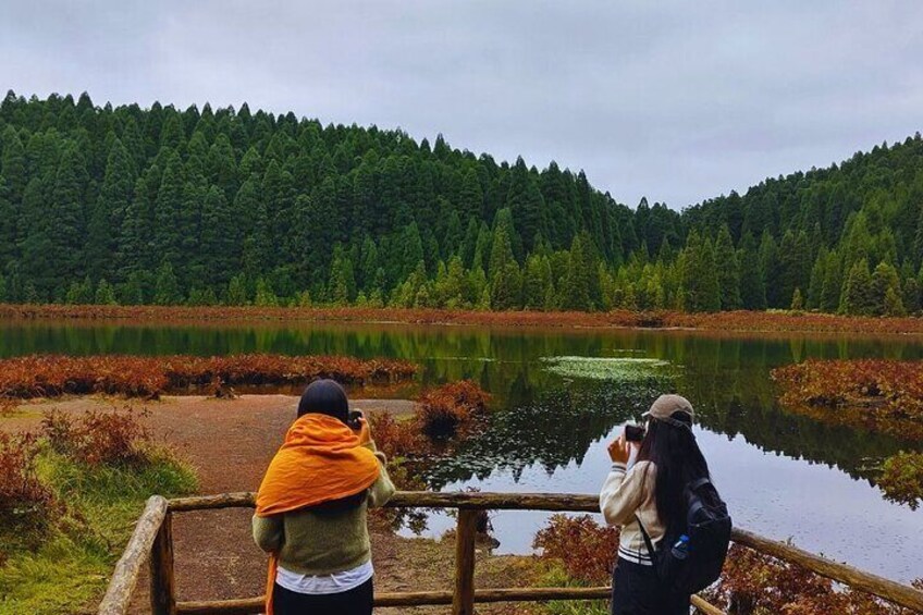 Zwei Personen fotografieren einen See, der von einem Wald umgeben ist. 5